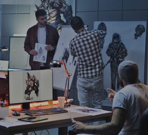 3 people in an art studio work on character designs, with sketches visible around them